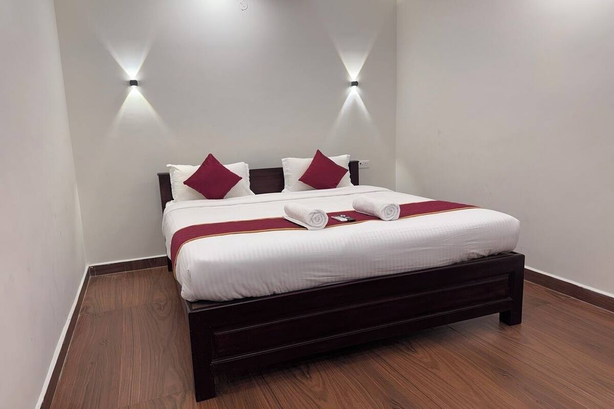 A neatly made bed with white bedding and red pillows, a wooden headboard, and wall-mounted lighting.