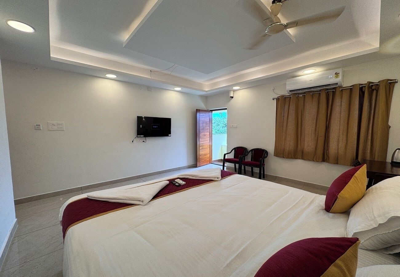 Ein Hotelzimmer mit einem großen Bett, einem an der Wand montierten Flachbildfernseher, einem Deckenventilator und einem Fenster mit Vorhängen.