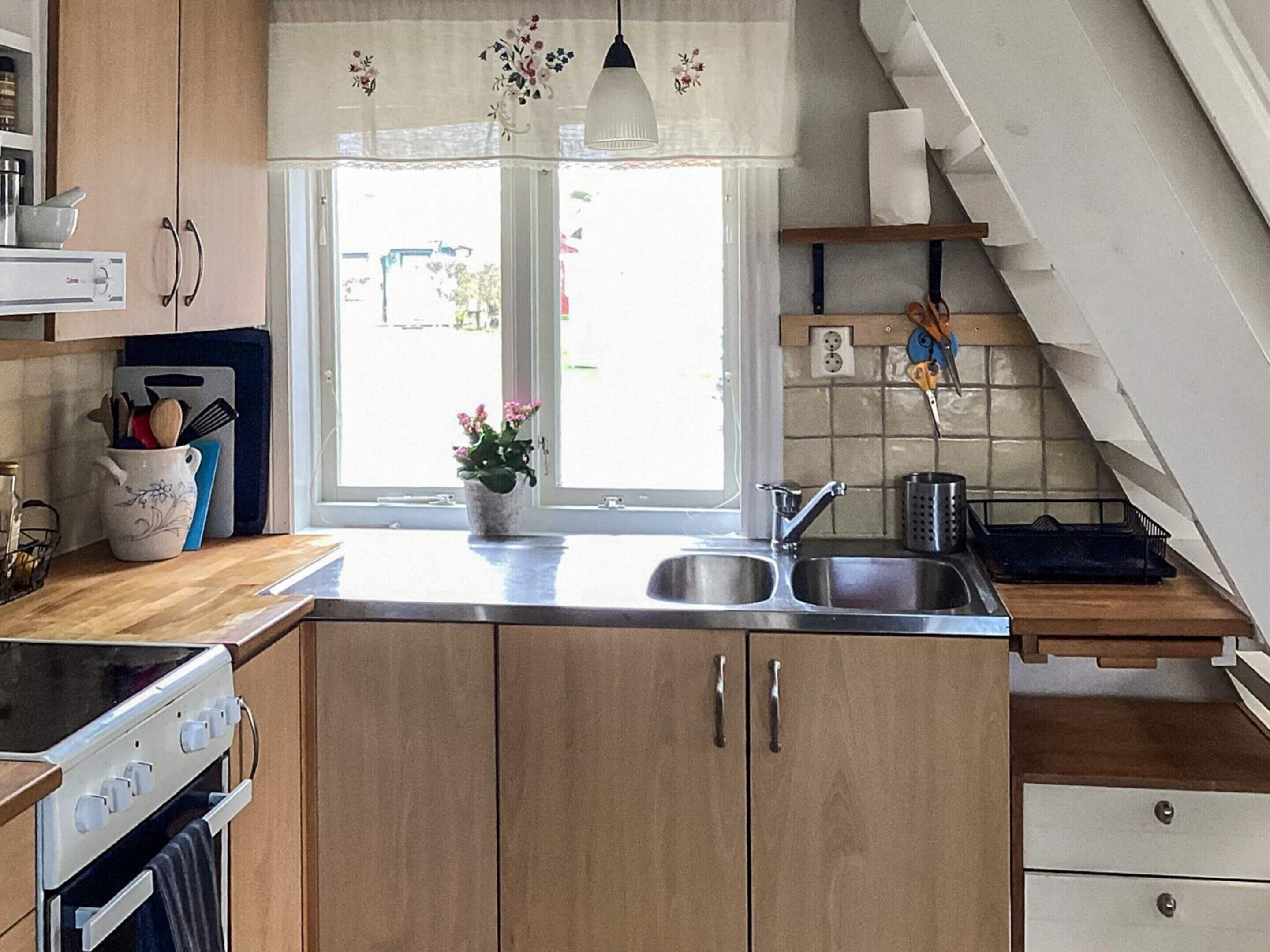 A kitchen with wooden cabinets, a stainless steel sink, a stove, and a window with a view of the outside.