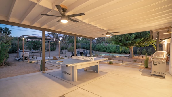 En udendørs patio med poolbord, ventilatorer i loftet og grill.