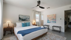 A hotel room with a bed, two bedside tables, a ceiling fan, a window with curtains, and artwork on the walls. - Pool | Spa | Sauna | Fire pit | Cold Plunge (Yucca Valley)