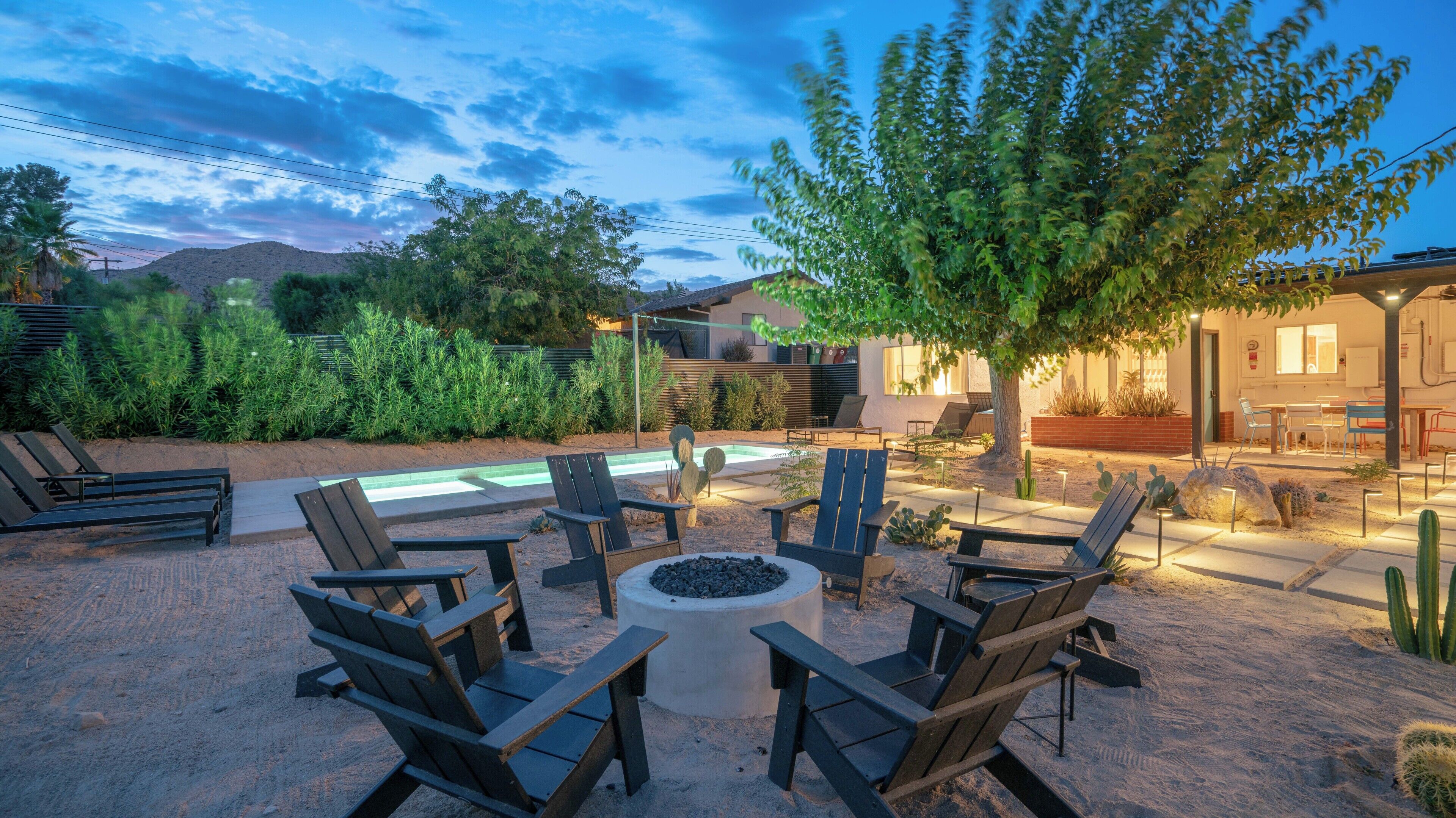 An outdoor seating area with chairs and a fire pit, surrounded by desert landscaping and a pool.