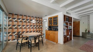 Une cuisine moderne avec un mur orné d’un motif géométrique, une table de salle à manger ronde entourée de chaises et des placards en bois intégrés.