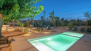 A swimming pool with a wooden deck, surrounded by desert plants and a pergola. - Pool | Spa | Sauna | Fire pit | Cold Plunge (Yucca Valley)