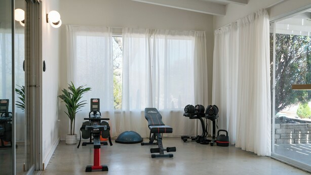 Une salle de sport à domicile équipée de matériel d’exercice, notamment un vélo d’appartement, un banc, des haltères et un kettlebell.