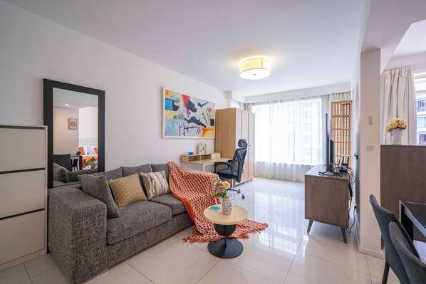 Een moderne woonkamer met een grijze bank, een ronde salontafel en een werkhoek.