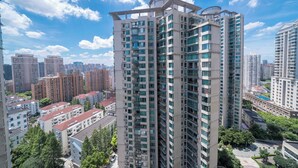A high-rise residential building with multiple balconies, surrounded by other high-rise buildings and greenery.