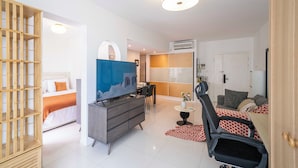 A modern hotel room with a bed, a TV, a desk, and a seating area.