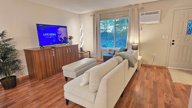 A living room with a sofa, a TV, a wooden cabinet, a potted plant, and a view of the outdoors through a window. - Downtown Chanhassen Townhome - 3 bedrooms (Chanhassen)