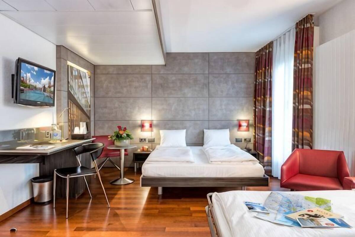 A modern hotel room with a bed, desk, chair, and a TV on the wall.
