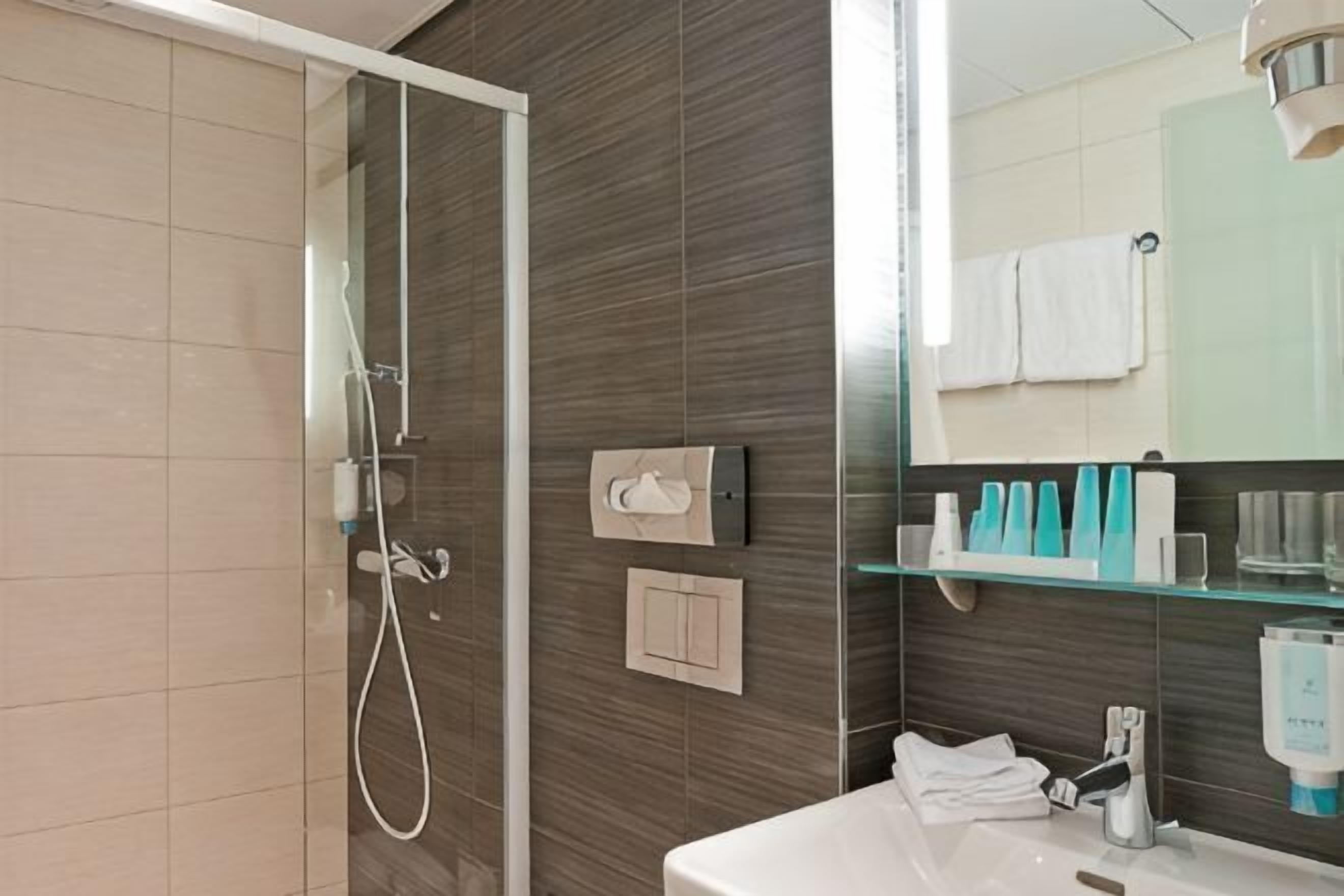 Ein Badezimmer mit Duschkabine aus Glas, Waschbecken, Spiegel und Pflegeprodukten auf einer Ablagefläche.