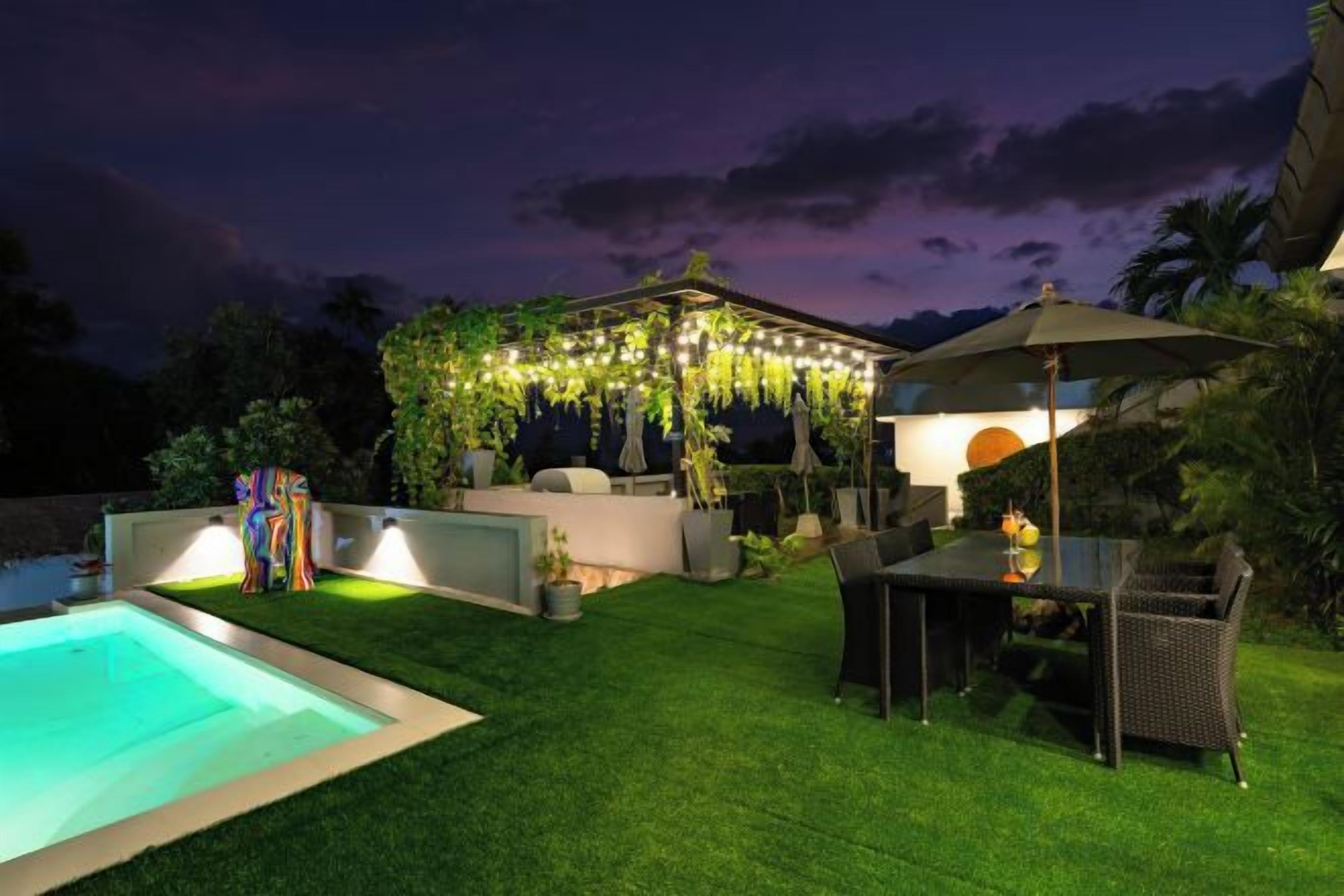 Um quintal com piscina, área de estar coberta com luzes pendentes e mesa com cadeiras.