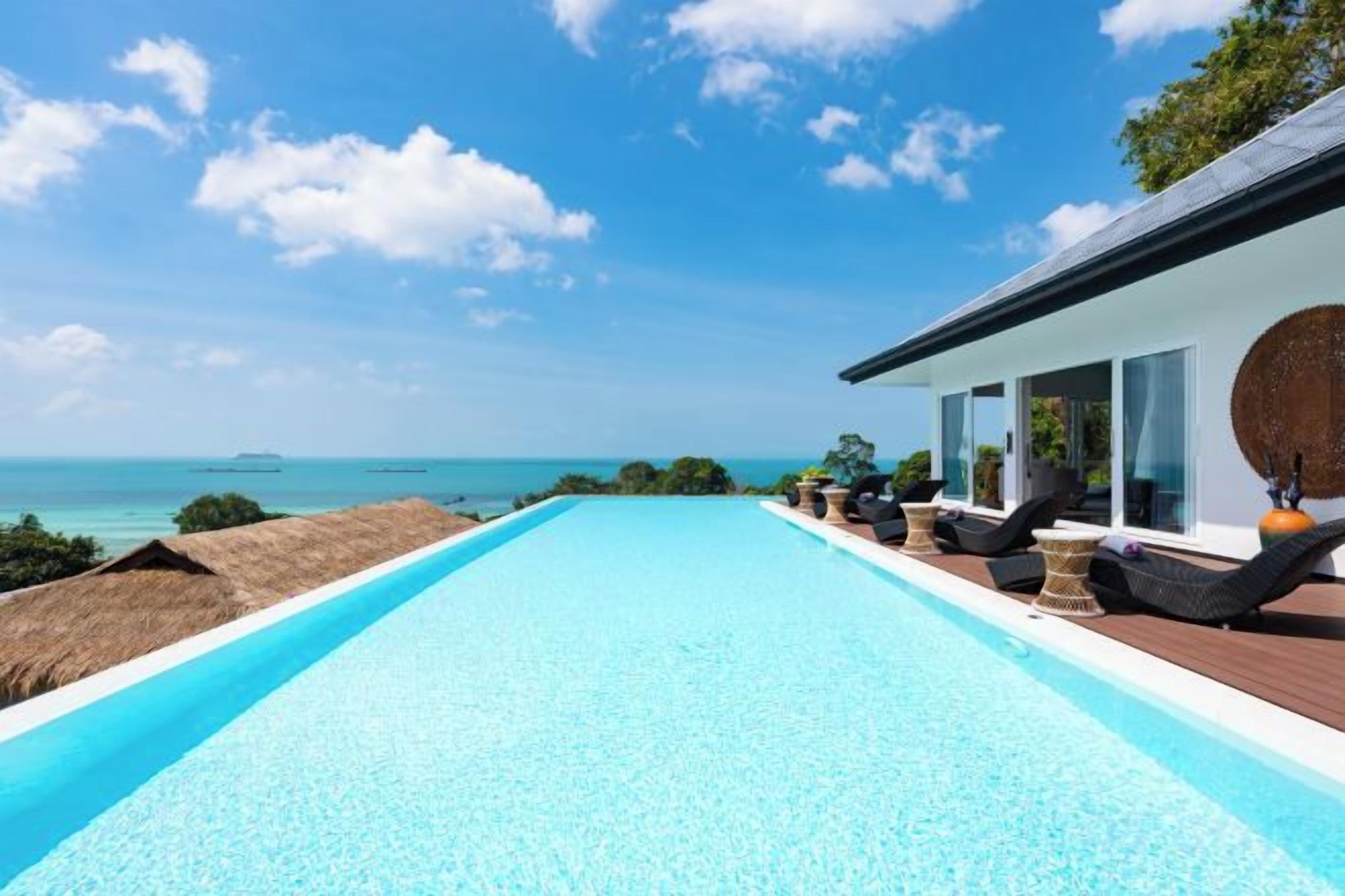 A swimming pool with a view of the sea, a covered deck area, and lounge chairs.