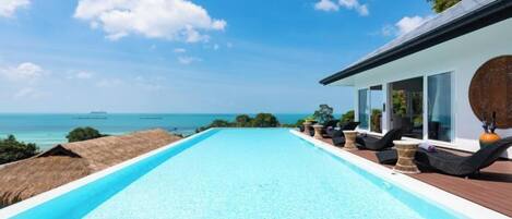 A swimming pool with a view of the sea, a covered deck area, and lounge chairs.