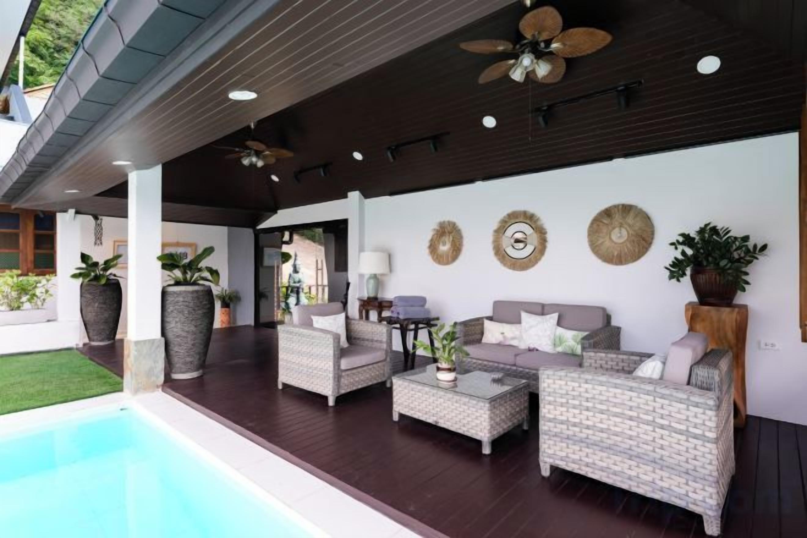 Zona relax esterna con mobili in vimini, piscina e decorazioni a parete.