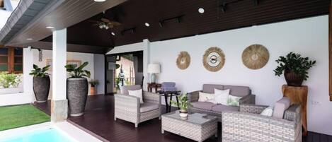 An outdoor lounge area with wicker furniture, a pool, and decorative wall art.