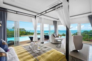 Une chambre dotée d’un grand lit, d’un coin salon avec vue sur l’océan et d’un balcon avec piscine.