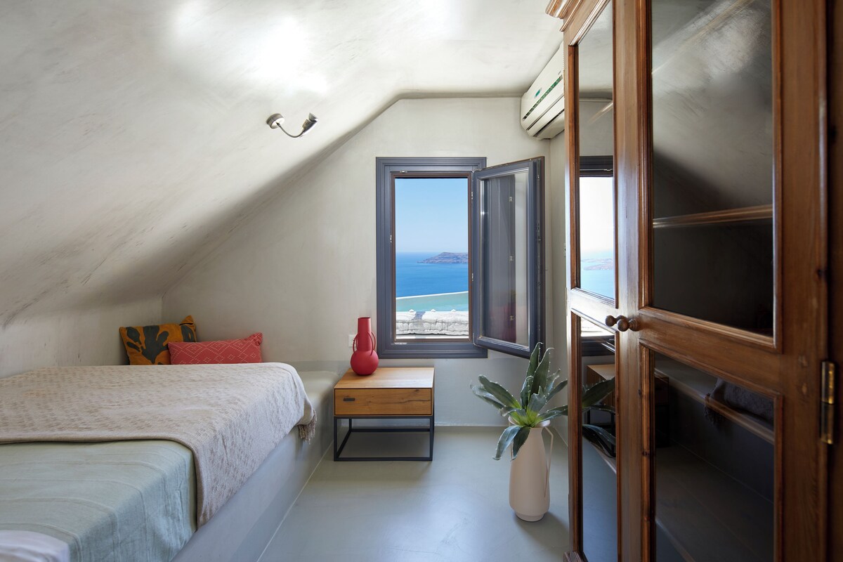 Un dormitorio con cama, una mesita de noche pequeña, una planta en maceta y una ventana con vista al mar.