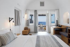 A modern hotel room with a large bed, a desk, and a view of the sea.