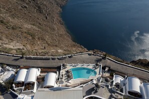 Une piscine sur le toit offre une vue dégagée sur la mer, et est entourée de structures cylindriques blanches, probablement des unités de climatisation, ainsi que d’une allée pavée.