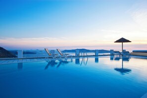 A pool with lounge chairs and a sun umbrella, surrounded by clear skies and distant landforms. - Santorini Princess Spa Hotel (Santorini)