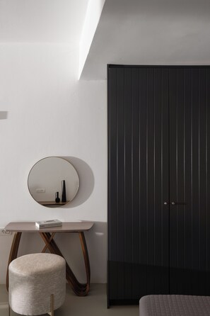 A modern bedroom with a large wardrobe, a round mirror, a small table, and a round ottoman. - Santorini Princess Spa Hotel (Santorini)