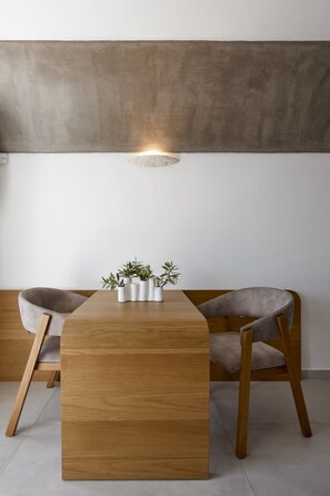 A modern dining area with a wooden table, two grey upholstered chairs, and a small potted plant arrangement. - Santorini Princess Spa Hotel (Santorini)