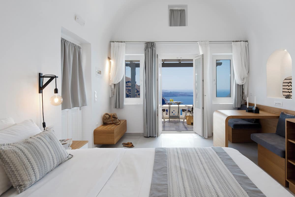 A modern hotel room with a large bed, a desk, and a view of the sea.