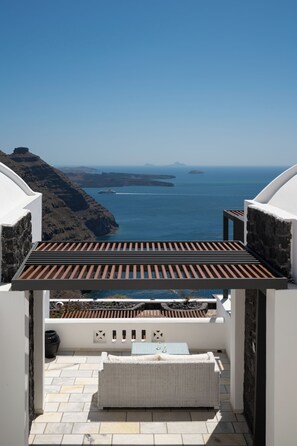 A balcony with a view of the sea, a wicker sofa, and a table.