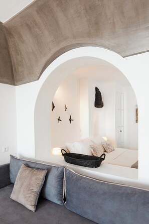 A modern room with a sofa, a bed, and a unique arched window. - Santorini Princess Spa Hotel (Santorini)