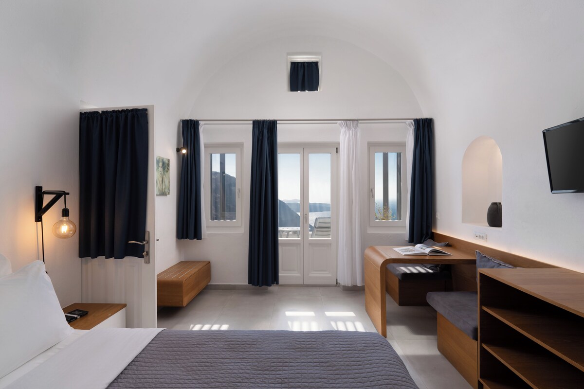 Una habitación de hotel moderna con cama, mesita de noche, lámpara, escritorio y vistas al exterior.