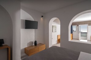 A modern bedroom with a bed, a wooden dresser, a flat-screen TV, and a balcony with a view.