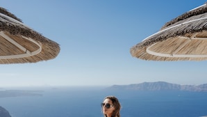 Une personne assise sur un balcon donnant sur une vue côtière, avec des parasols en chaume.