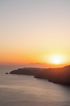 Un paysage côtier avec un coucher de soleil, une mer calme et des reliefs terrestres lointains.