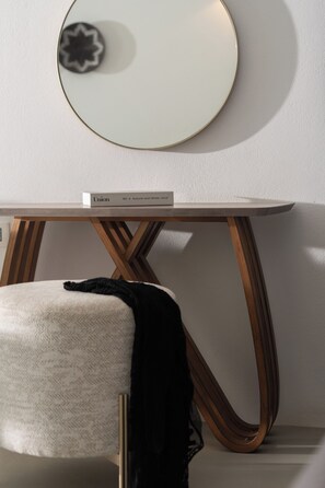 A modern room with a round mirror on the wall, a white chair with a black throw, and a table with wooden legs and a white top. - Santorini Princess Spa Hotel (Santorini)