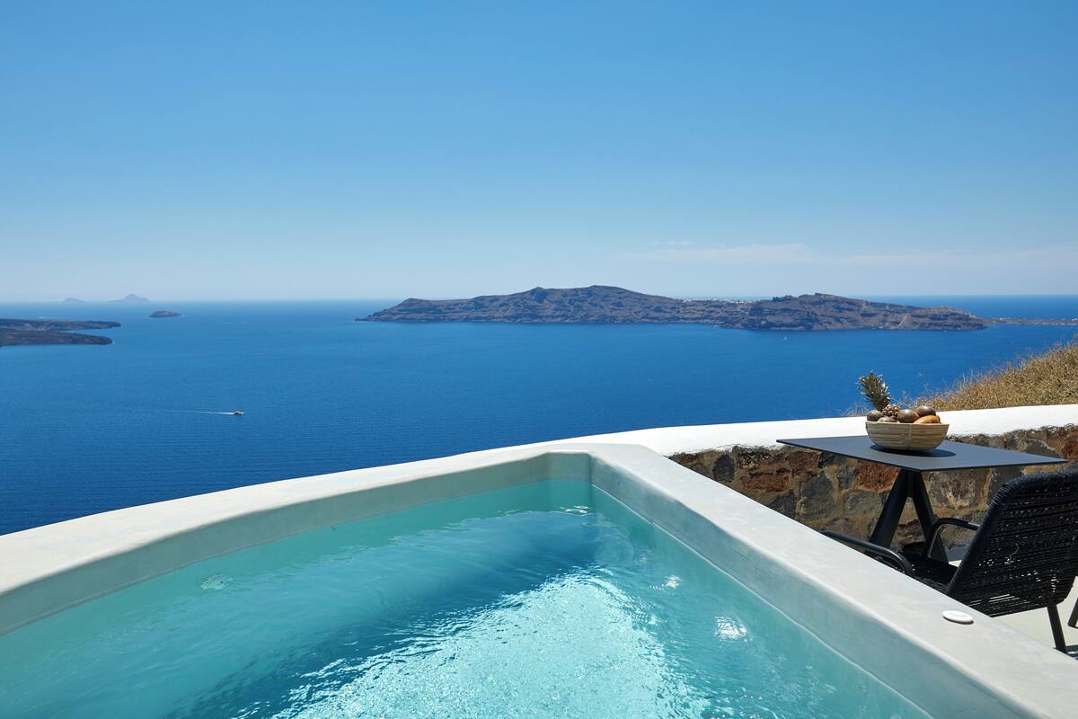 A pool with a view of the sea and a small table with a fruit bowl.