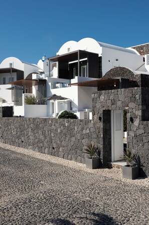 Um edifício moderno branco com entrada em parede de pedra, janelas amplas e céu azul claro.