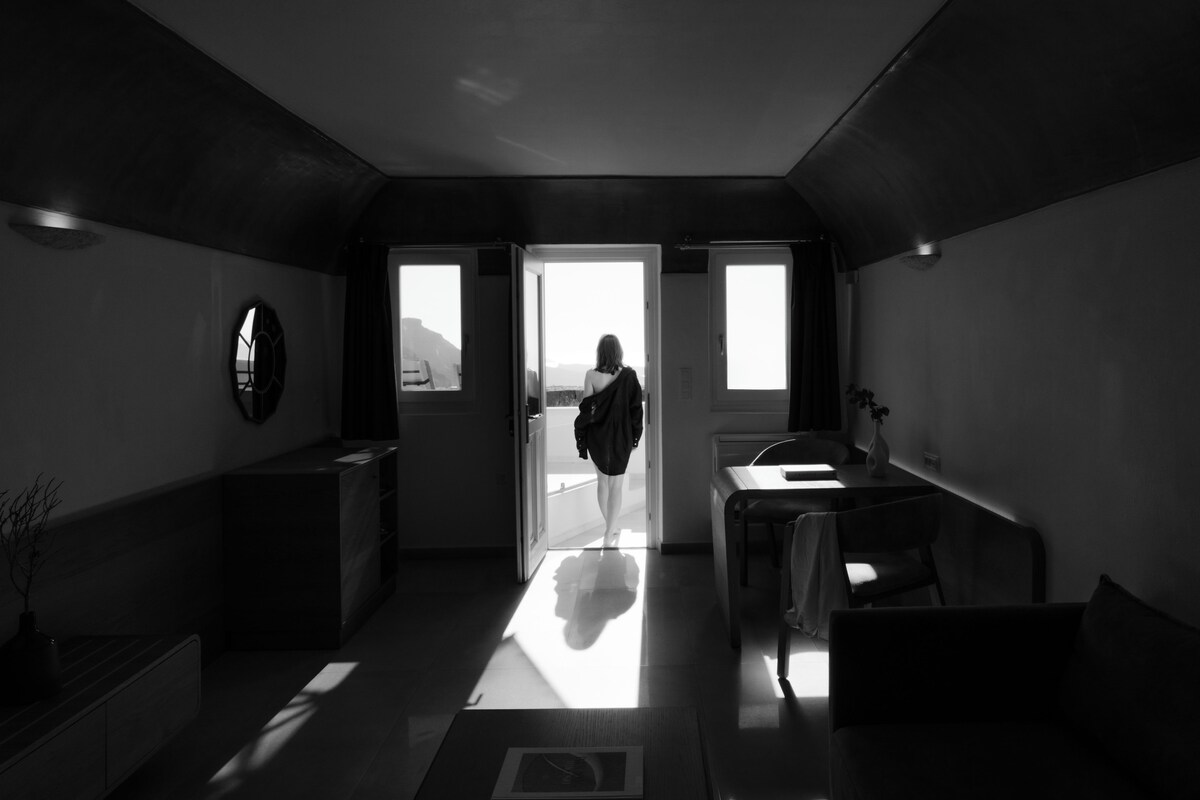 Habitación de hotel moderna y minimalista con un ventanal grande, un televisor de pantalla plana y un pequeño rincón de descanso.