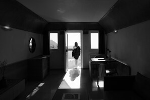 Habitación de hotel moderna y minimalista con un ventanal grande, un televisor de pantalla plana y un pequeño rincón de descanso.