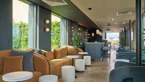 A modern hotel lobby with a sofa, round tables, and a bar area. - The Store (Oxford)