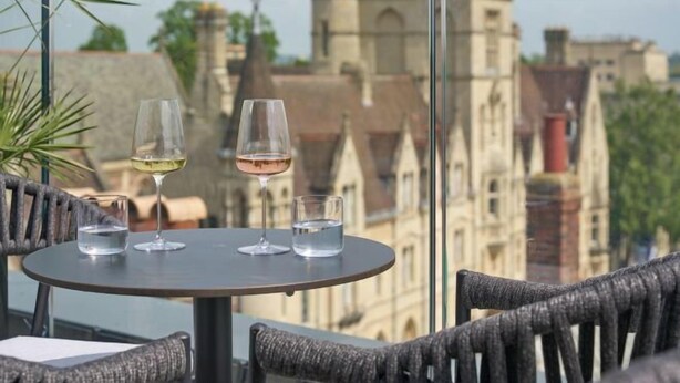 A balcony with a table set for two, overlooking a historic building with a tower. - The Store (Oxford)