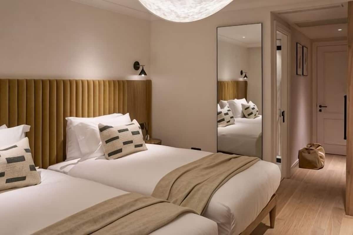 Hotellihuone, jossa on kaksi sänkyä, suuri peili, puinen sängynpääty ja ovi, joka johtaa toiseen huoneeseen.