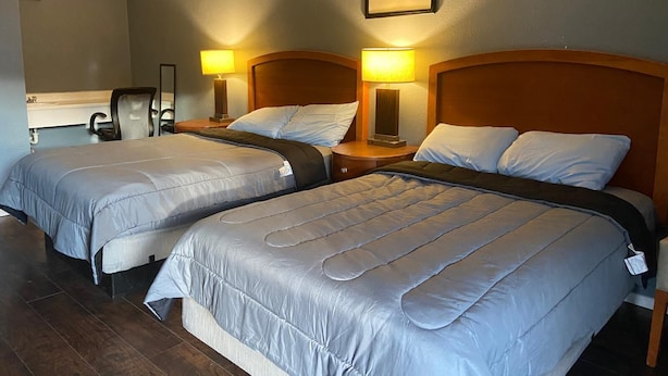 A hotel room with two beds, each with a wooden headboard, a desk with a chair, and two bedside lamps. - Glendale Inn (Glendale)