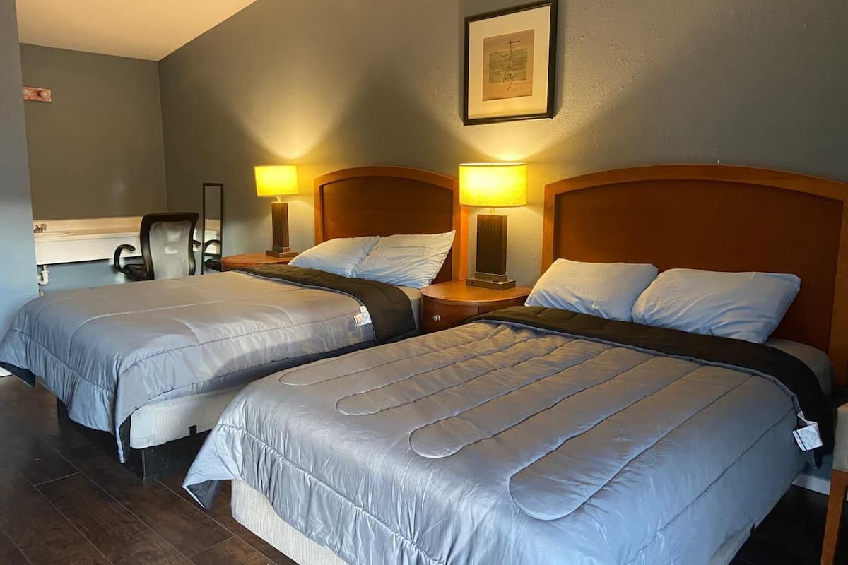 Habitación de hotel con dos camas, cada una con cabecero de madera, un escritorio con silla y dos lámparas de noche.