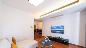 Ένα μοντέρνο σαλόνι με έναν λευκό καναπέ, ένα στρογγυλό τραπεζάκι σαλονιού και μια τηλεόραση επίπεδης οθόνης τοποθετημένη στον τοίχο.