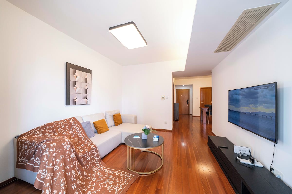 A modern living room with a sofa, a coffee table, and a flat-screen TV mounted on the wall.
