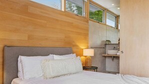 Un dormitorio moderno con una cama grande, una mesita de noche con lámpara y vistas al baño.