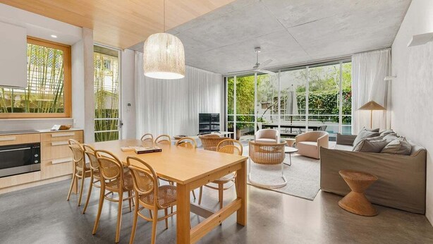 Una cocina moderna con comedor, ventanas amplias y una sala de estar con sofá y lámpara.