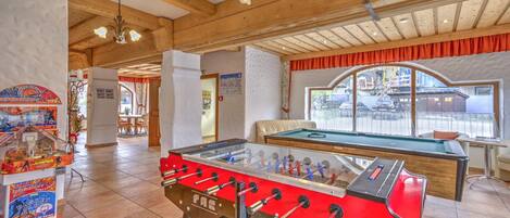 A room with a foosball table, a pool table, and a basketball arcade.