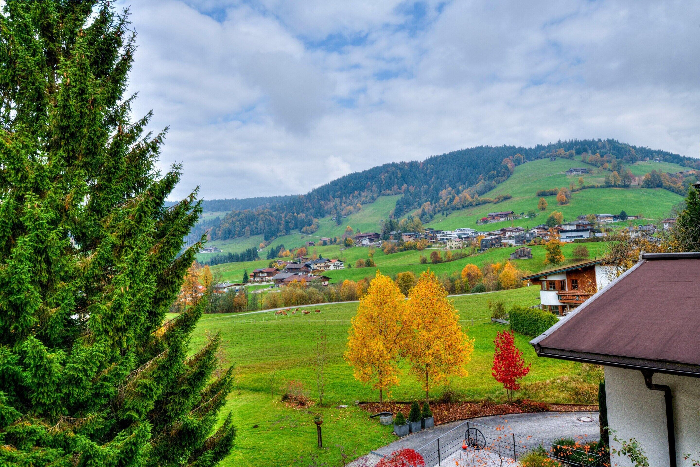 Paesaggio rurale con una casa, campi verdi e una collina sullo sfondo.